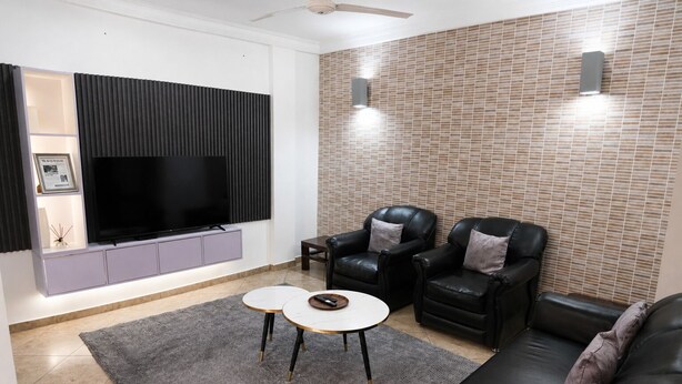 Una sala de estar moderna con una televisión de pantalla plana, dos sillones de cuero, un sofá y una mesa de centro.