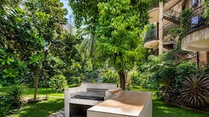 Un patio con una fogata, un espacio de descanso y abundante vegetación.