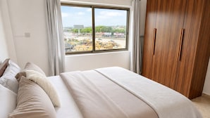 Un dormitorio con cama, armario de madera y ventana con vista a maquinaria de construcción.