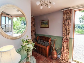 A room with a wooden bench, a vase with flowers, a mirror, and a painting on the wall. - Captains Barn (Tiverton)