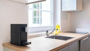 Una cocina con encimera de madera, una cafetera negra, un fregadero y una ventana con vistas a la vegetación.