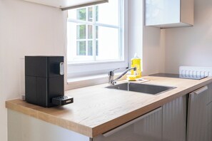 Eine Küche mit einer Holzausstattung, einer schwarzen Kaffeemaschine, einem Spülbecken und einem Fenster mit Blick ins Grüne.