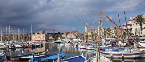 Una marina con varias embarcaciones amarradas, una grúa al fondo y edificios a lo largo del paseo marítimo.