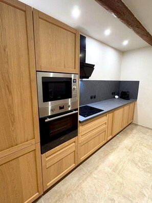 A modern kitchen with wooden cabinets, a built-in oven, a microwave, and a stovetop. - The Little House — An Air-Conditioned Provençal Retreat (Caumont-sur-Durance)