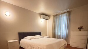 Un dormitorio con cama, mesita de noche, cómoda y aire acondicionado.