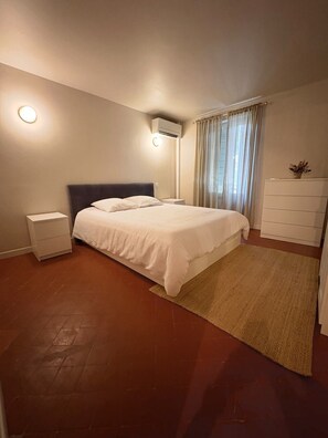 A bedroom with a bed, nightstand, dresser, and an air conditioning unit. - The Little House — An Air-Conditioned Provençal Retreat (Caumont-sur-Durance)