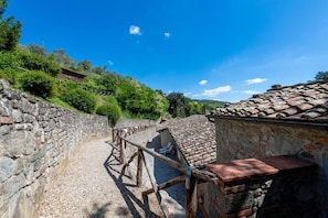 Un pati amb parets de pedra, una banca de fusta, un edifici petit amb teulada de rajola i una escala de pedra.
