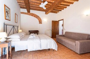 Ein Schlafzimmer mit einem Bett, einem Sofa, einem Schreibtisch mit Lampe, einem Deckenventilator und einem Backsteinbogen.
