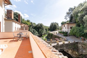 Una terraza con mesa y sillas, con vistas a un patio que tiene un puente de piedra y vegetación.