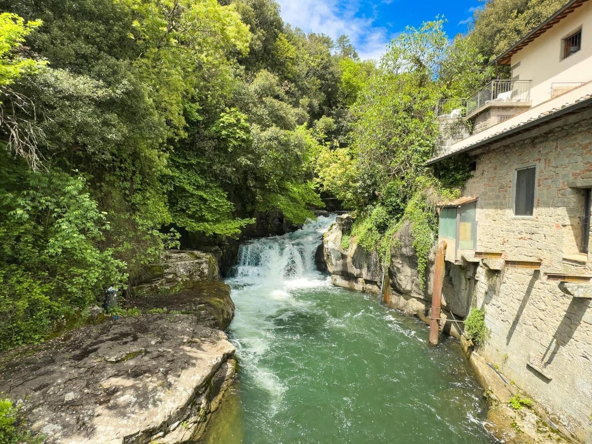 Un edificio in pietra con una cascata in una verdeggiante valle.