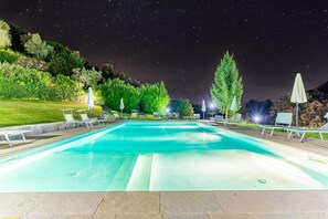 Ein Schwimmbecken mit Liegestühlen und Sonnenschirmen, umgeben von Bäumen und Hügeln.