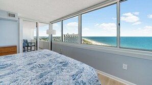 Quarto com uma grande janela que oferece vista para a praia e o oceano.