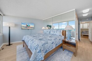 Ein Schlafzimmer mit einem Bett, Nachttischlampen, einem Fernseher, einem Spiegel und einem Fenster mit Blick.