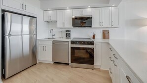 Uma cozinha moderna com armários brancos, eletrodomésticos de aço inoxidável e piso de madeira.