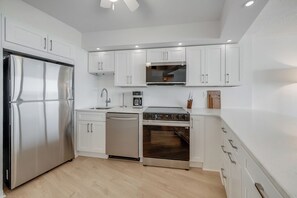 A modern kitchen with white cabinets, stainless steel appliances, and a wooden floor. - Antigua 1103 by Seaside Vacations & Sales (Ocean City)