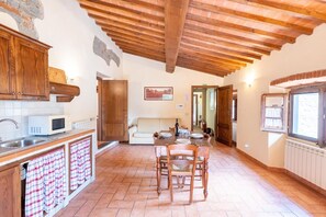 Una cocina con armarios de madera, un microondas blanco, una mesa de comedor con sillas y un piso de baldosas.