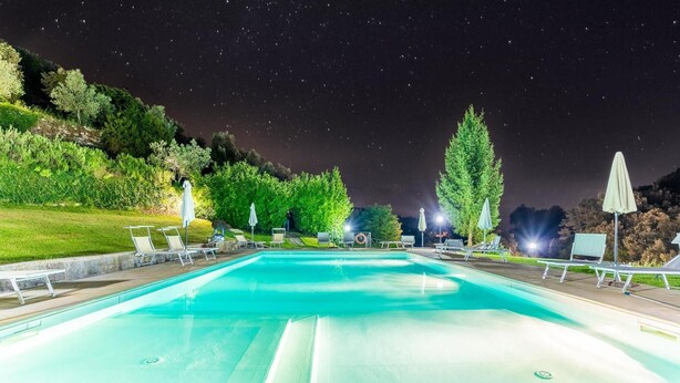 A swimming pool with lounge chairs and umbrellas, surrounded by trees and hills.