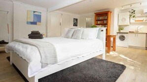 Een slaapkamer met een bed, een nachtkastje, een boekenkast en een wasmachine in de aangrenzende ruimte.