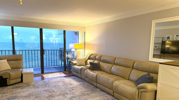 Un salon avec un canapé, une table basse, une lampe et un téléviseur. Il y a un balcon avec vue sur la mer.