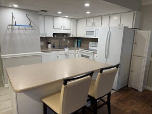 A modern kitchen with white cabinets, a central island, and a refrigerator. - Turning Tides: 1 bed, 2 bath direct luxury oceanfront condo in Garden City (Murrells Inlet)