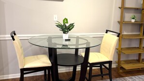 Un coin repas avec une table en verre entourée de chaises, un ventilateur de plafond et une bibliothèque en bois.