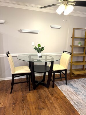 A dining area with a glass table surrounded by chairs, a ceiling fan, and a wooden bookshelf. - Turning Tides: 1 bed, 2 bath direct luxury oceanfront condo in Garden City (Murrells Inlet)