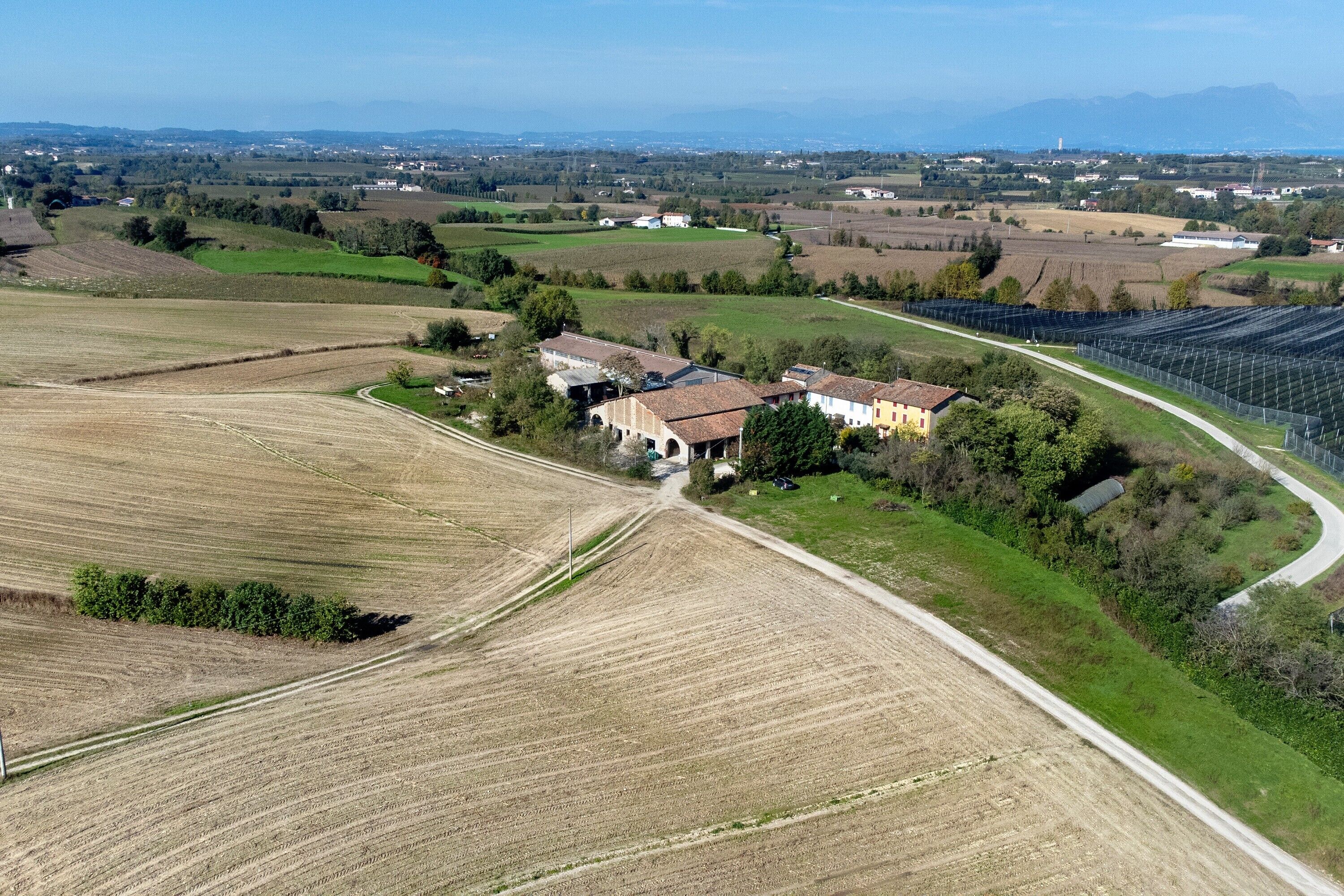 Une vue aérienne d’un paysage rural, avec des champs, une route et un bâtiment doté d’un toit rouge.