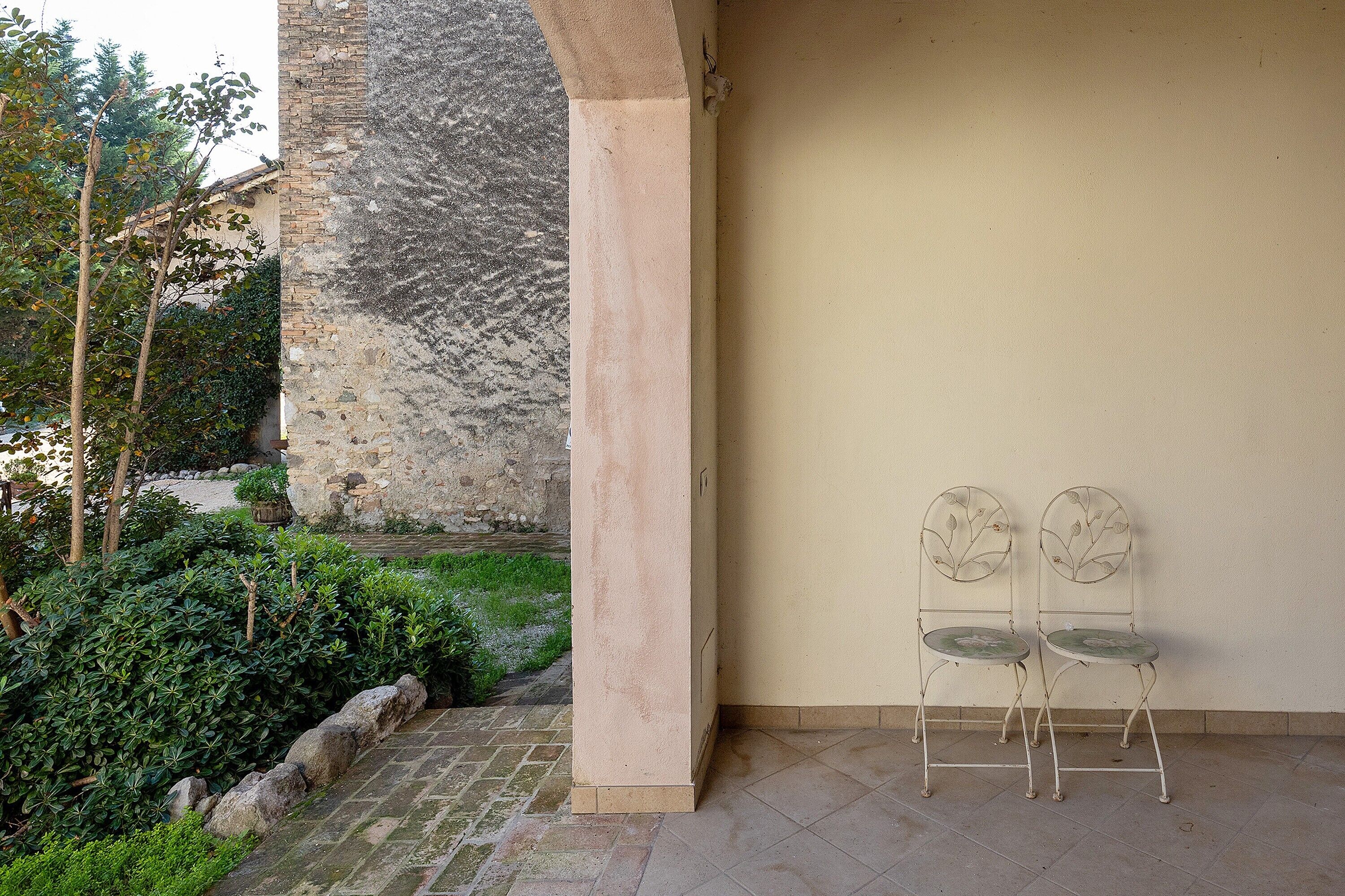 Un patio con un muro de piedra, dos sillas de metal y suelo de baldosas.