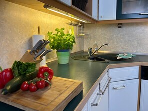 A kitchen with a wooden cutting board, a potted basil plant, a sink, and a stainless steel faucet.
