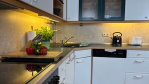 Una cocina moderna con armarios blancos, encimera de acero inoxidable, lavavajillas y hervidor.