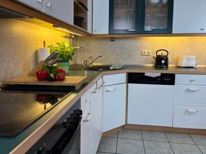 A modern kitchen with white cabinets, a stainless steel countertop, a dishwasher, and a kettle.