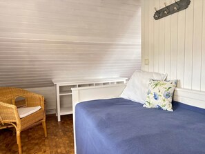 A room with a bed, a white console table, a wicker chair, and a wall-mounted shelf.
