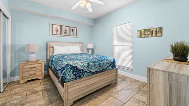 A bedroom with a bed, nightstands, a ceiling fan, a window with blinds, and a wall-mounted sign. - Ocean-view escape w/ pools, hot tub & beach access (Panama City Beach)