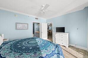 Un dormitorio con una cama, un aparador, un ventilador de techo y un televisor.
