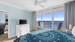 A bedroom with a large bed, a TV on a dresser, and a balcony with a view of the ocean. - Ocean-view escape w/ pools, hot tub & beach access (Panama City Beach)