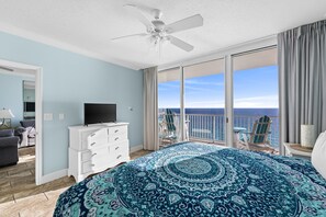 Ein Schlafzimmer mit einem großen Bett, einem Fernseher auf einer Kommode und einem Balkon mit Meerblick.