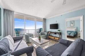 A modern living room with a large window, a flat-screen TV, and a cozy seating area. - Ocean-view escape w/ pools, hot tub & beach access (Panama City Beach)