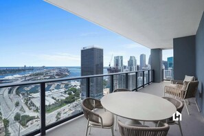 Un balcon avec vue sur la ville et l’eau, aménagé avec des fauteuils et une table en osier.