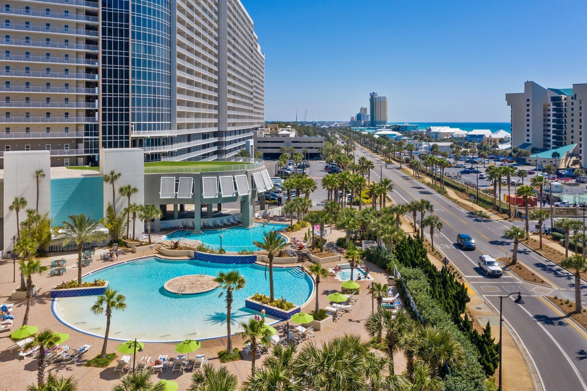 A hotel with a large pool, palm trees, and a view of the beach.