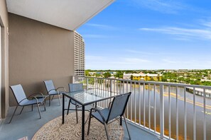 Ein Balkon mit Glastisch und Stühlen, der auf ein Gewässer und eine ferne Skyline blickt.