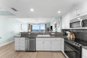 A modern kitchen with a dishwasher, stove, microwave, and white cabinets. - 20th Floor Beachfront Retreat | Sleeps 8 (Panama City Beach)