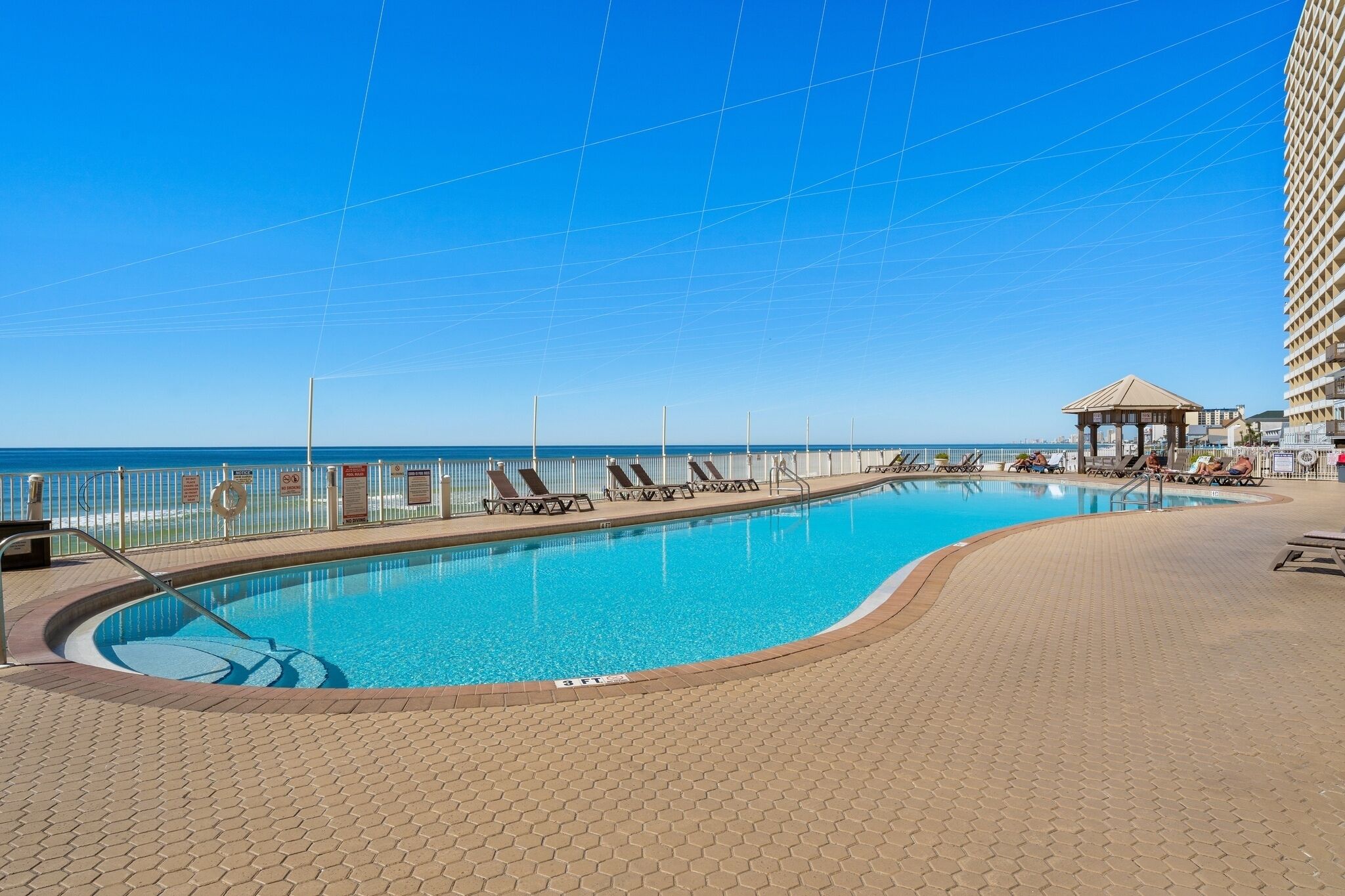 Ein Swimmingpool mit Liegestühlen, einer Laube und Blick aufs Meer.