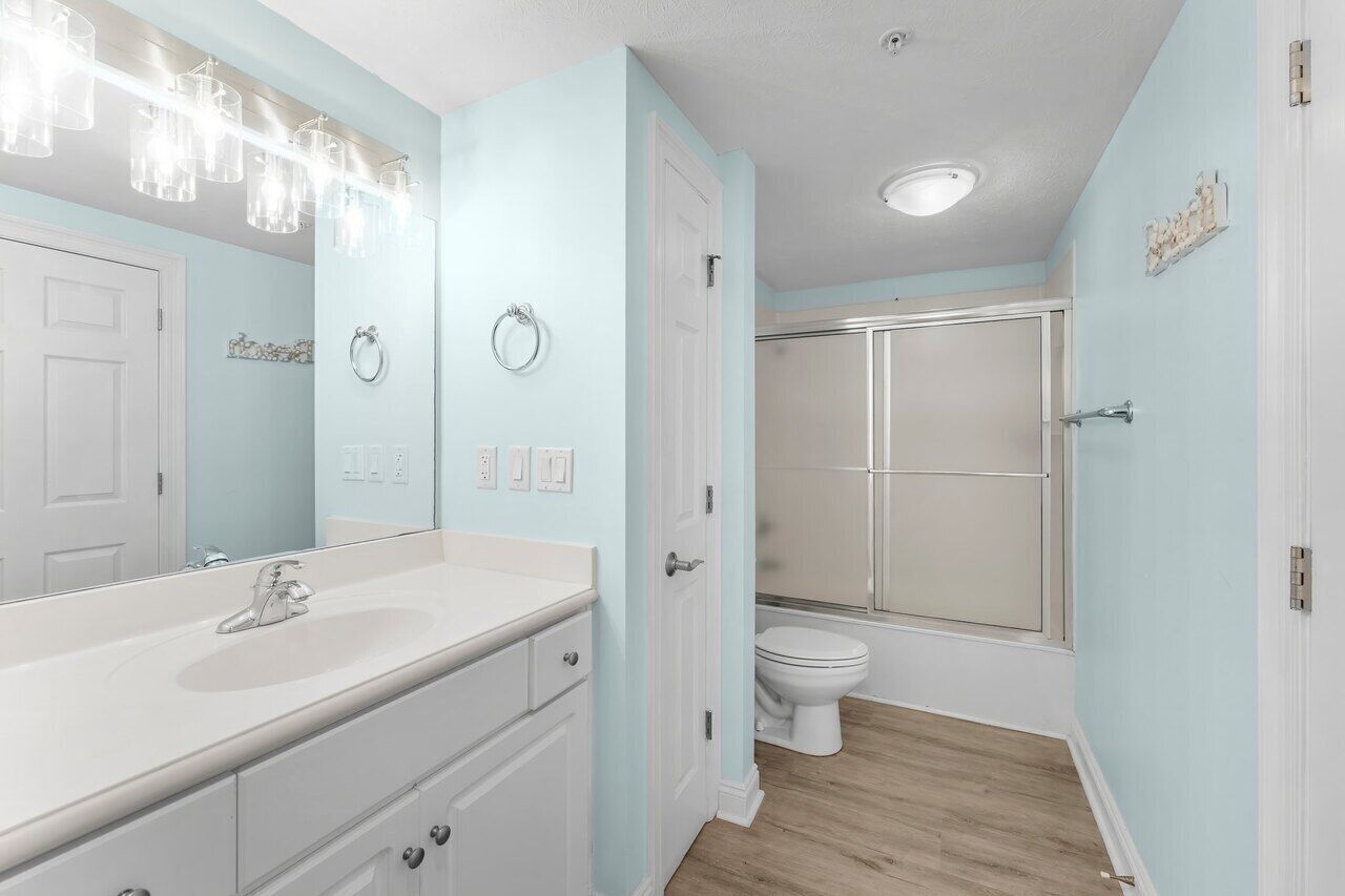 A bathroom with a white vanity, a large mirror, a shower, and a toilet.