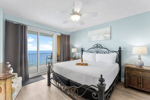 A bedroom with a bed, a ceiling fan, a nightstand, a lamp, a view of the ocean, and a balcony. - 20th Floor Beachfront Retreat | Sleeps 8 (Panama City Beach)