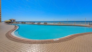 En swimmingpool med ett parasoll, solstolar och utsikt över havet.