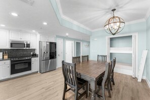 A modern kitchen with white cabinets, stainless steel appliances, and a wooden dining table. - 20th Floor Beachfront Retreat | Sleeps 8 (Panama City Beach)