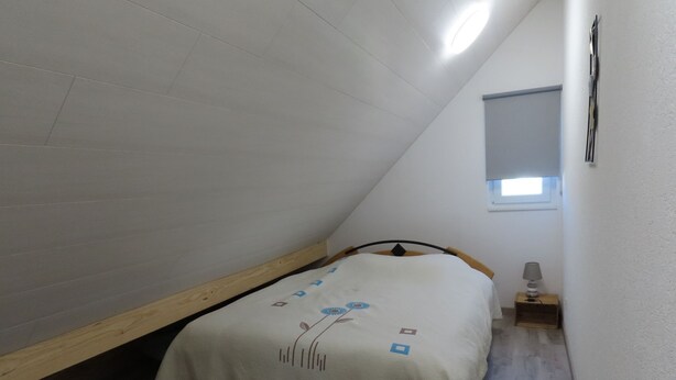 A small, sloped room with a single bed, a nightstand, and a window. - Appartement - Les P'tits Loups, (Courtedoux), by Interhome (Courtedoux)