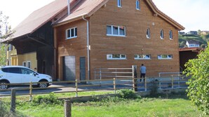 A two-story wooden building with a sloped roof, multiple windows, and a gated entrance. - Appartement - Les P'tits Loups, (Courtedoux), by Interhome (Courtedoux)