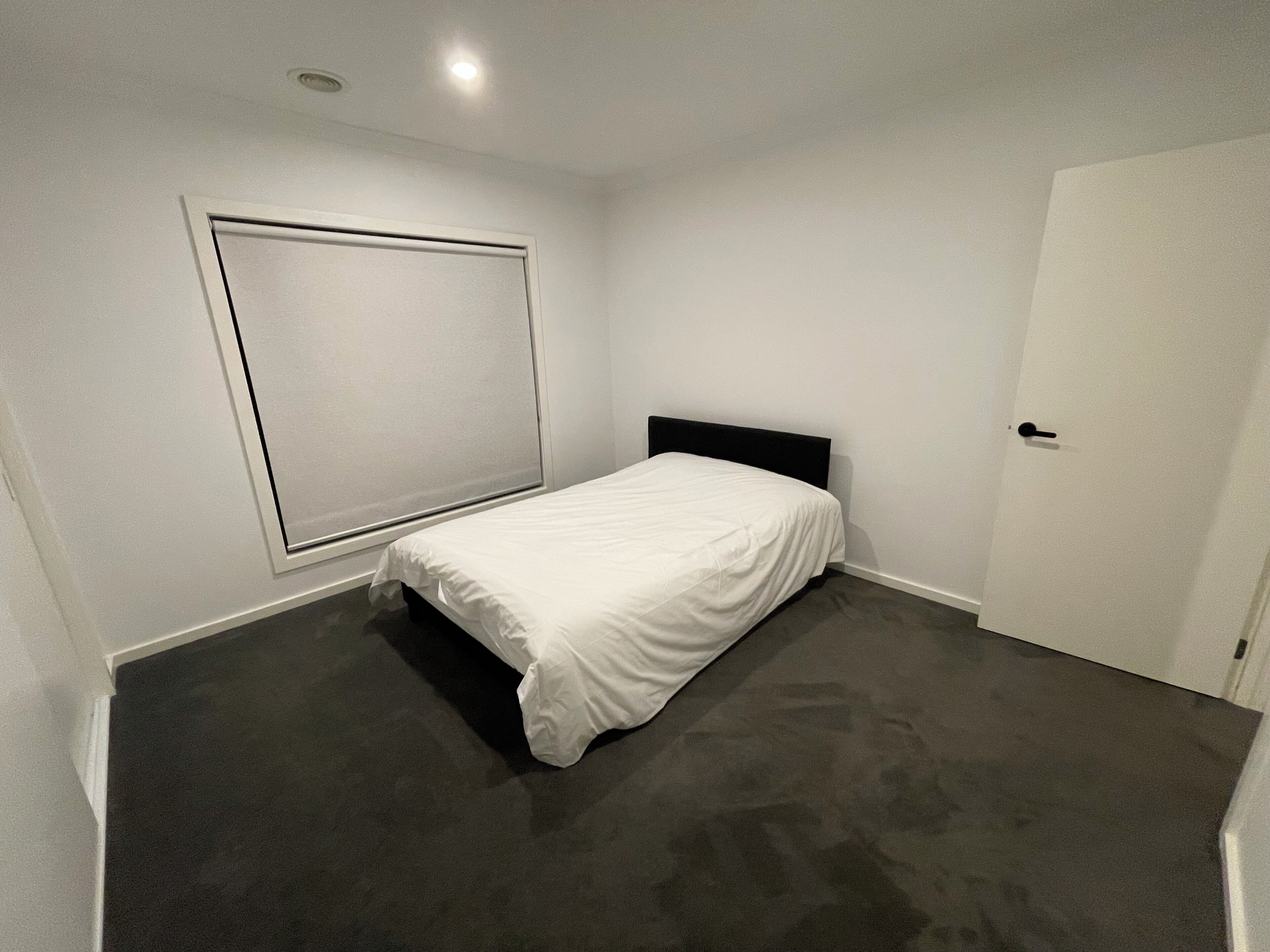 Un dormitorio con una cama individual, una puerta y un ventanal con persianas.