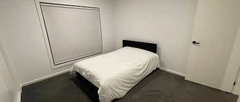 Une chambre avec un lit simple, une porte et une fenĂȘtre avec des stores.